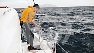 crew deckhand in yellow sweatshirt of a large sailing catamaran adjusting fenders and ropes