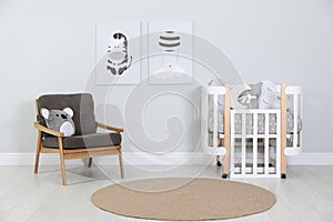 Crib and armchair near wall with pictures in cozy baby room. Interior design