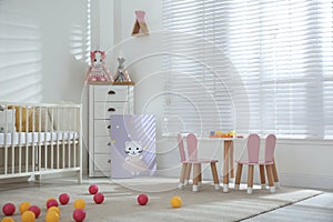 Crib, table and chairs with bunny ears in stylish baby room interior