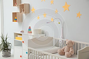 Crib with toy bear and mobile in baby room interior