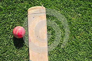 Cricket bat and ball on a green grass. Cricket equipments isolated on a green background.