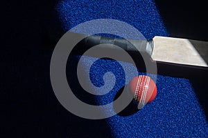 Cricket bat and ball with natural lighting on blue background