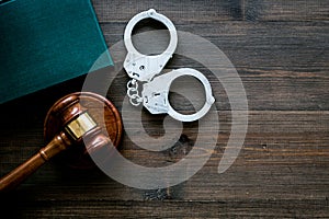 Crime concept. Metal handcuffs near judge gavel and law book on dark wooden background top view copy space