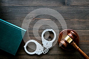 Crime concept. Metal handcuffs near judge gavel and law book on dark wooden background top view copy space