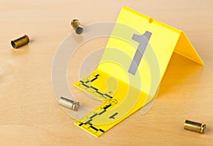 Crime scene investigation CSI evidence marker with empty, fired 9mm bullet casings on wood floor background at crime scene -