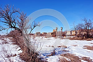 Crimean coquina rock blocks ruined farm walls, two water towers, dry weathered grass field covered with snow, elderberry bushes