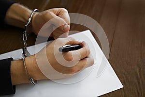 Criminal in handcuffs writing confession at desk