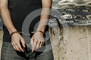 Criminal in jail. A handcuffed man stands against a barbed wire wall. Prisons. Law and order. Handcuffs