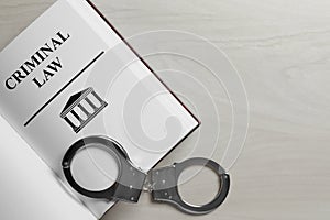 Criminal Law book and handcuffs on wooden background, top view. Space for text