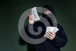 Criminal man in black hood holding banknotes mockup and counting money in hand, mask thief robber committing committed