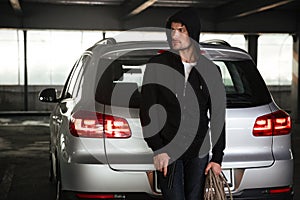 Criminal man with gun and rope standing near the car