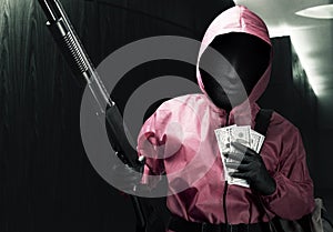 Criminal man in pink uniform and a hidden mask holding the shotgun and carrying a bag of money after the robbery