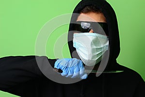 Criminal in a medical surgical mask and sunglasses dressed in black with a hood holds a knife in his hand