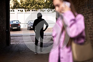 Criminal stalking a woman alone in dark street alley. Female is talking on phone