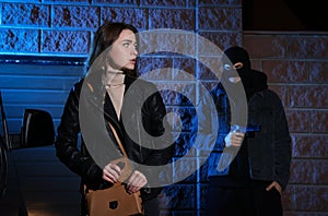 Criminal threatening young woman with gun outdoors at night. Self defense concept