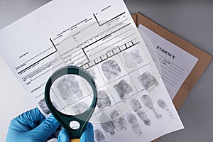 Criminalist in blue gloves examines fingerprint card with  magnifying glass