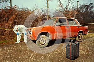 Criminologist technician collecting evidences from burned car on location of crime
