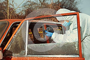 Criminologist technician collecting evidences from burned car on location of crime