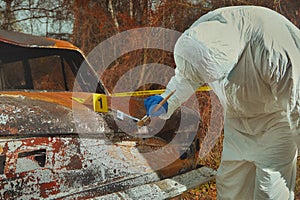 Criminologist technician collecting evidences from burned car on location of crime