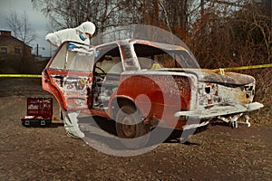 Criminologist technician collecting evidences from burned car on location of crime