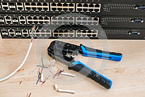 Crimper, utp Ethernet cable are on the background of internet switches. The pieces of the cable are next to the network photo