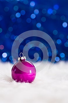 Crimson Christmas ball on white fur with garland lights on blue
