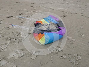 Crinkled kite in rainbowcolors with white threads laying on the beach of Velsen Netherlands