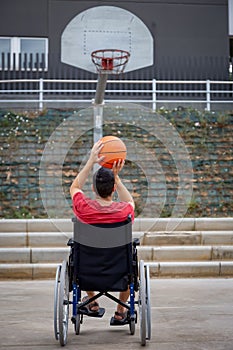 Cripple basketball player in wheelchair plays basketball on open air ground