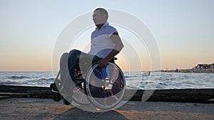 Crippled man pushes himself on background sunset and enjoying nature sea, disabled person sitting in wheelchair