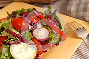 A crisp healthy salad with a fork on a yellow plate with rustic