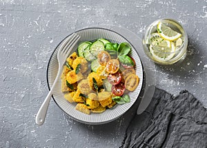 Crispy baked slices of polenta with sage butter and vegetables cucumbers, tomatoes, basil salad on a gray background, top view.