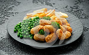 Crispy Battered scampi nuggets served on slate plate with potato chips and green peas photo