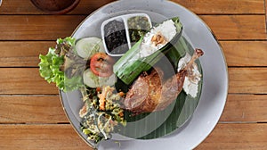 Crispy black fried duck with rice covered in banana leaf, some veggetable and special mash chili photo