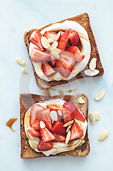 Crispy breakfast toasts with ricotta, strawberries and almonds on white marble background