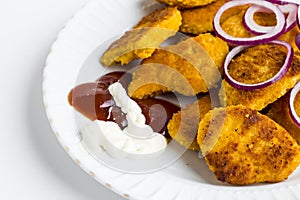 Crispy chicken nuggets in the plate with onion rings,ketchup,mayonnaise and fork.