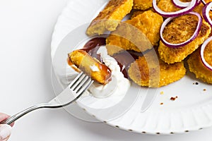 Crispy chicken nuggets in the plate with onion rings,ketchup,mayonnaise and fork.