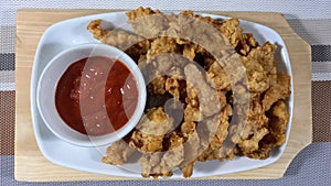 Crispy Chicken Popcorn together With Chlli Sauce In A White Bowl, On A Rectangle White Plate, Overhead View On A Wooden Board