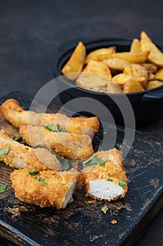 Crispy chicken and potatoes on dark table
