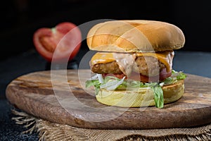 Crispy Chicken Sandwich or burger with cabbage, tomato, lettuce leaf, melted cheese and mayonnaise isolated on wooden board with