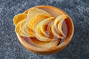 Crispy chips in a wooden bowl on a gray dark table. Snack.