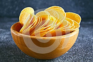 Crispy chips in a wooden bowl on a gray dark table. Snack.