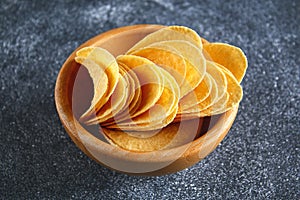 Crispy chips in a wooden bowl on a gray dark table. Snack.