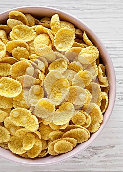 Crispy corn flakes in a pink bowl for breakfast over white wooden background, top view. Flat lay, overhead, from above. Close-up