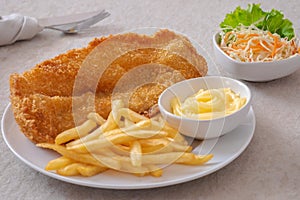 Crispy fish and chips on white plate and vegetable salad in bowl