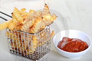 Crispy French Fries in a wire fryer basket with Ketchup