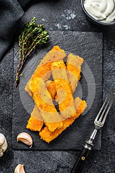 Crispy fried fish fingers with breadcrumbs served with sauce tartar. Black background. Top view