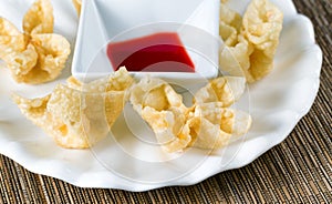 Crispy fried wanton and sauce in white bowl on bamboo mat