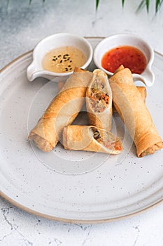 Crispy golden fried vegetable spring rolls with fresh ingredients served with soy and sweet and sour sauce in an