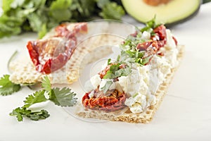 Crispy low-calorie wheat crackers with curd cheese and sun-dried tomatoes on a background of avocado and greens