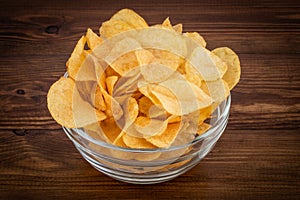 Crispy potato chips in bowl on wooden background